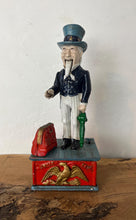 Load image into Gallery viewer, This mechanical coin bank features Uncle Sam, the national personification of the U.S. government. It is made of cast iron and hand-painted. When a coin is placed in Uncle Sam's hand and a lever is pressed, his arm moves down, depositing the coin into a bag and then into the bank's base; his beard also moves.