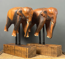 Load image into Gallery viewer, The elephants are carved from rosewood, with a two-tone finish that highlights the details of the skin and body. The carvings are detailed, showing the texture of the skin, the shape of the ears, and the tusks.