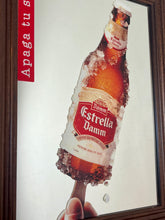 Load image into Gallery viewer, The main image is a unique graphic of an ice-encrusted Estrella Damm bottle held like a popsicle or ice lolly by a hand.