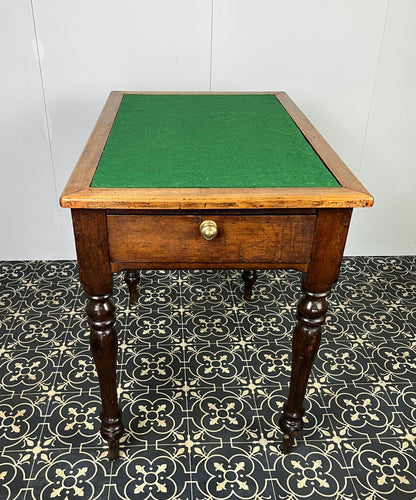 The table consists of a mahogany top edging of a rectangular shape with a central green baize surface. This leads down a mahogany panel with a small drawer with an original brass handle, leading to four turned legs supported by sleek, elegant feet.