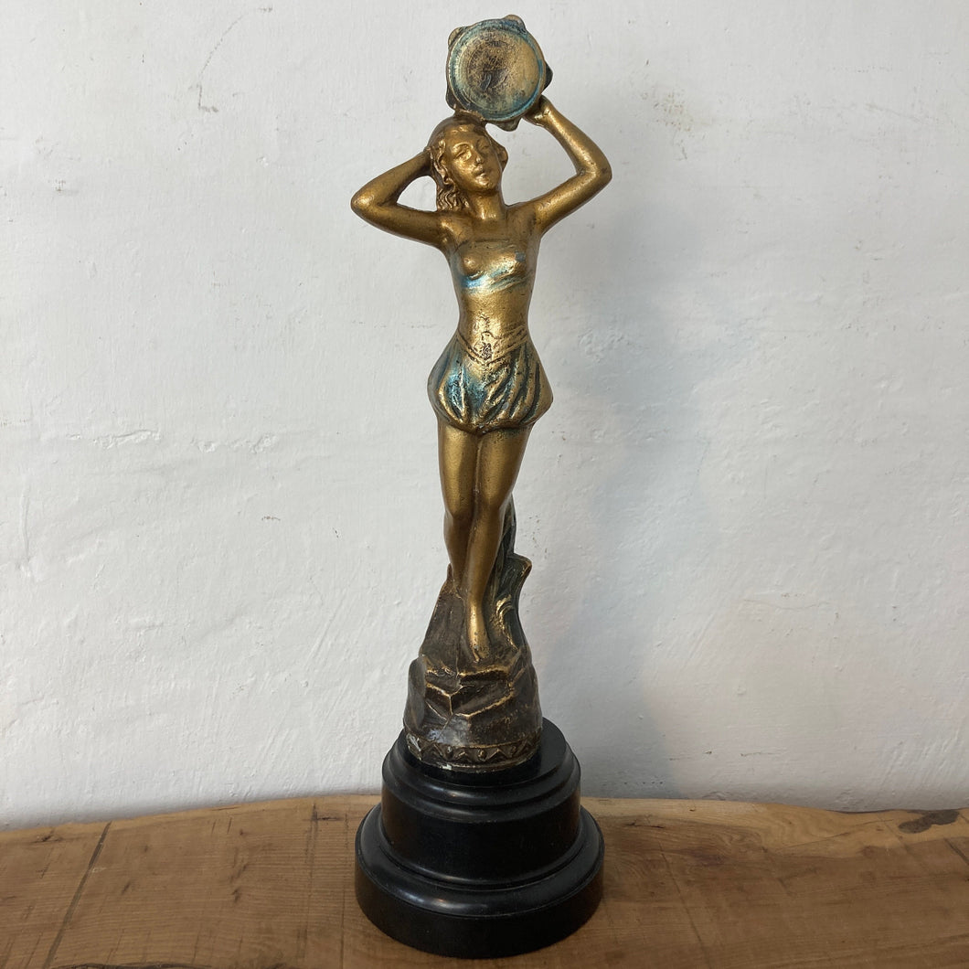 This stunning Art Deco piece features a glamorous lady flapper in superb, intricate detail. She is wearing skimpy clothing and holding up her decorative tambourines at the top, posing standing on a rocky floor to create a stand-out antique design.
