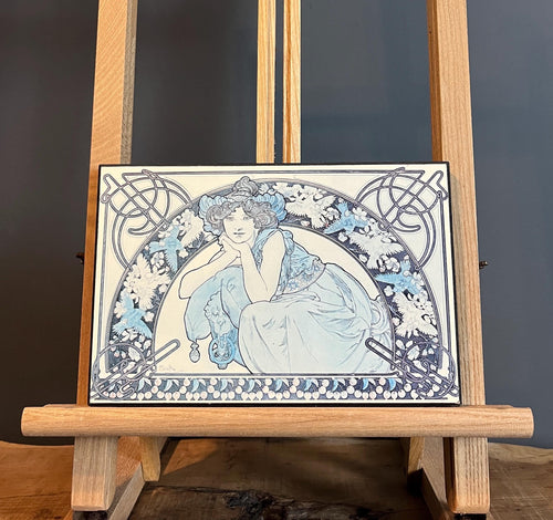 This vintage art nouveau wooden wall plaque, with a blue effect, is a unique piece of art. It features an elegant lady wearing an attractive headdress, her hair tied up, and a selection of glamorous clothing.