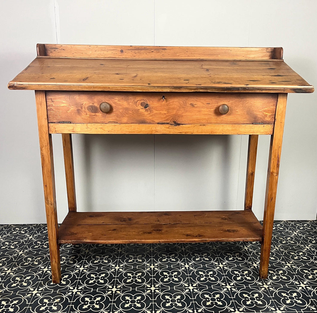 Excellent pitch pine clerk desk with raised back and sloped writing surface over a single fall-front cupboard with key, raised on square supports united by under-tier two plank pine shelf.