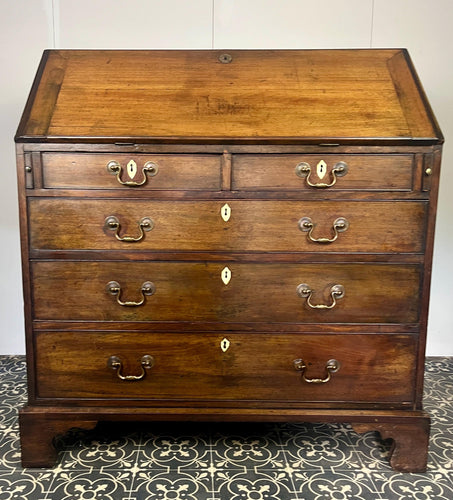 The antique mahogany bureau has a fall front that opens to reveal a writing surface. Its elegant fitted interior consists of six pigeon holes, five drawers on either side, and a central cupboard with Roman columns with a gold detail sitting on desirable runners