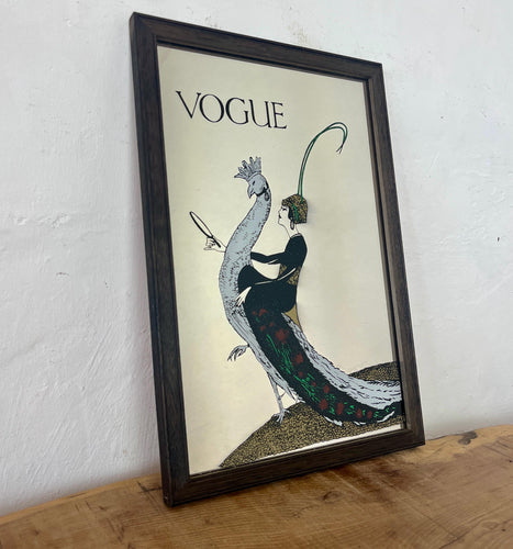 This exquisite vintage item showcases a captivating peacock design that draws inspiration from Vogue's April 1918 magazine cover. It depicts a sophisticated lady adorned with a fashionable headband, holding a mirror above the Vogue designer logo, all encased within a delicate border.