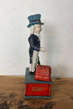 Load image into Gallery viewer, This mechanical coin bank features Uncle Sam, the national personification of the U.S. government. It is made of cast iron and hand-painted. When a coin is placed in Uncle Sam&#39;s hand and a lever is pressed, his arm moves down, depositing the coin into a bag and then into the bank&#39;s base; his beard also moves.
