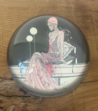Load image into Gallery viewer, Beautiful vintage glass paperweight in Art Deco style, featuring an illustration of a lady in a pink dress and headpiece. This particular style, often associated with the roaring twenties, is characterised by its elegant and sophisticated portrayal of women, usually referred to as flapper ladies or Gatsby ladies.
