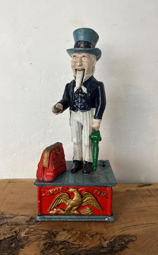 This mechanical coin bank features Uncle Sam, the national personification of the U.S. government. It is made of cast iron and hand-painted. When a coin is placed in Uncle Sam's hand and a lever is pressed, his arm moves down, depositing the coin into a bag and then into the bank's base; his beard also moves.