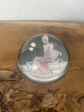 Load image into Gallery viewer, Beautiful vintage glass paperweight in Art Deco style, featuring an illustration of a lady in a pink dress and headpiece. This particular style, often associated with the roaring twenties, is characterised by its elegant and sophisticated portrayal of women, usually referred to as flapper ladies or Gatsby ladies.
