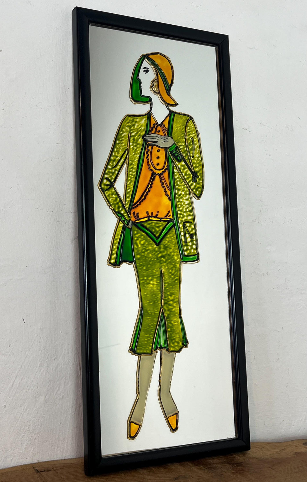 The mirror reflects the iconic Art Deco style, characterized by geometric shapes, streamlined forms, and vibrant colors, popular in the 1920s and 1930s. The depicted figure is a quintessential symbol of the Roaring Twenties.