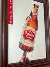 Load image into Gallery viewer, The main image is a unique graphic of an ice-encrusted Estrella Damm bottle held like a popsicle or ice lolly by a hand.
