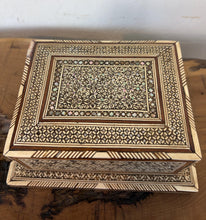 Load image into Gallery viewer, This stunning Vintage Middle Eastern Marquetry Cigarette Box features incredibly detailed, handcrafted geometric star patterns and micro-mosaic detailing. Combining traditional Khatam kari technique with natural wood, bone, and iridescent mother-of-pearl inlays, it rests on a prominent tiered pedestal base. High-quality boxes like this from the mid-20th century often feature hidden compartments or internal mechanical music boxes. It makes a sophisticated addition to any tobacciana collection.
