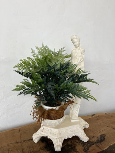 The sculpture is carved from white alabaster stone. The woman's face is delicate and feminine, with high cheekbones, a small nose and full lips. She is depicted in a flowing gown. Next to her is a shallow pot with beautiful detail on the outside.