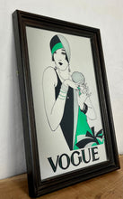 Load image into Gallery viewer, The photo features a woman wearing a stunning art deco dress and hat with block colors of black, green, and grey. She has a chic short bob haircut and is accessorized with stacked bracelets on both arms. The Vogue logo is displayed at the bottom.
