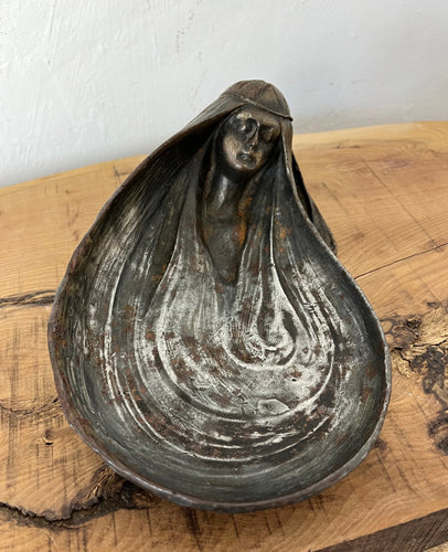 A drop-shaped metal bowl with a woman's head as a detail. The bowl is in art nouveau style, and the woman has long hair and a dreamy face—the bowl is a mixture of different tones of silver grey and sins of vintage patina.