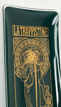 Load image into Gallery viewer, The picture shows a vintage glass tray with deep green background and Alphonse Mucha&#39;s painting La Trapisttine in gold. Depicts a young woman dressed in a religious habit with a calm and serene expression. One of her hands is on a bottle.
