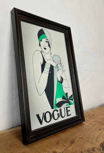 The photo features a woman wearing a stunning art deco dress and hat with block colors of black, green, and grey. She has a chic short bob haircut and is accessorized with stacked bracelets on both arms. The Vogue logo is displayed at the bottom.