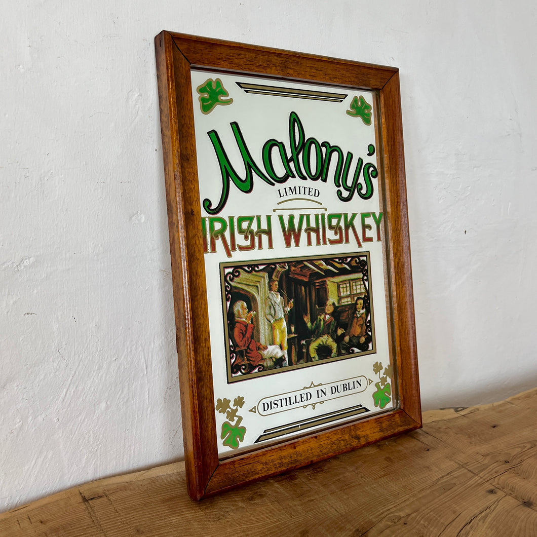 The mirror is beautifully designed with vibrant fonts in a multi-coloured tone, reminiscent of the Irish flag. The image captures the essence of the old days with a fireside scene and a pretty border designed with three-leaf clovers.