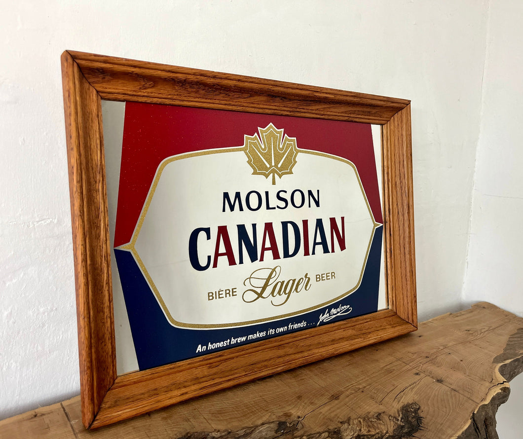 Striking red and blue designs, a gold maple leaf, and a detailed gold border, all complemented by a sleek pine frame. The Molson slogan is at the bottom.