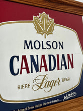 Load image into Gallery viewer, Striking red and blue designs, a gold maple leaf, and a detailed gold border, all complemented by a sleek pine frame. The Molson slogan is at the bottom.
