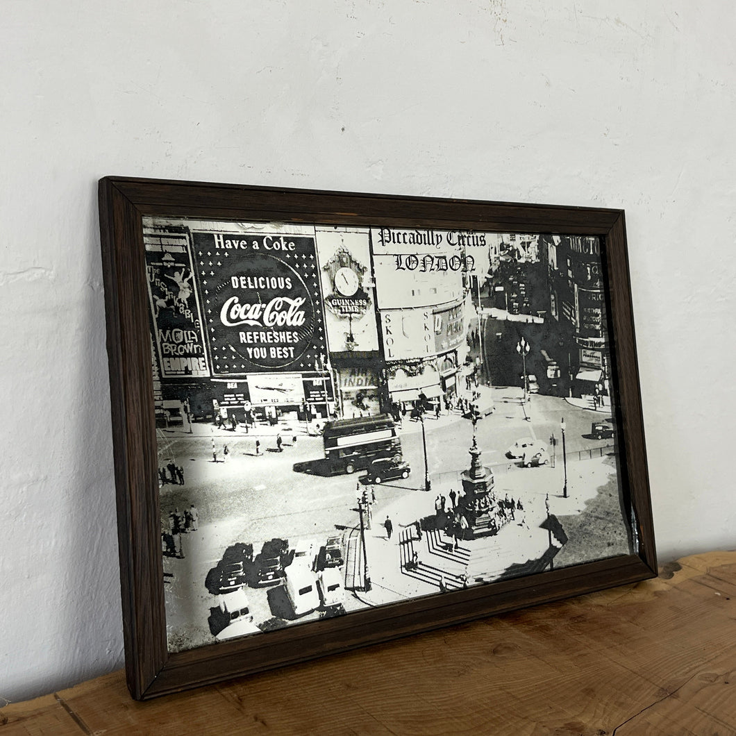 The artwork depicts a beautiful landscape design of Piccadilly Circus in a noir effect. The vintage image showcases the famous London landmark with its advertisement screens and the road that features vintage black cabs and iconic buses
